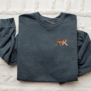 May include: A dark gray sweatshirt with a small embroidered tiger on the left chest. The tiger is orange and black.