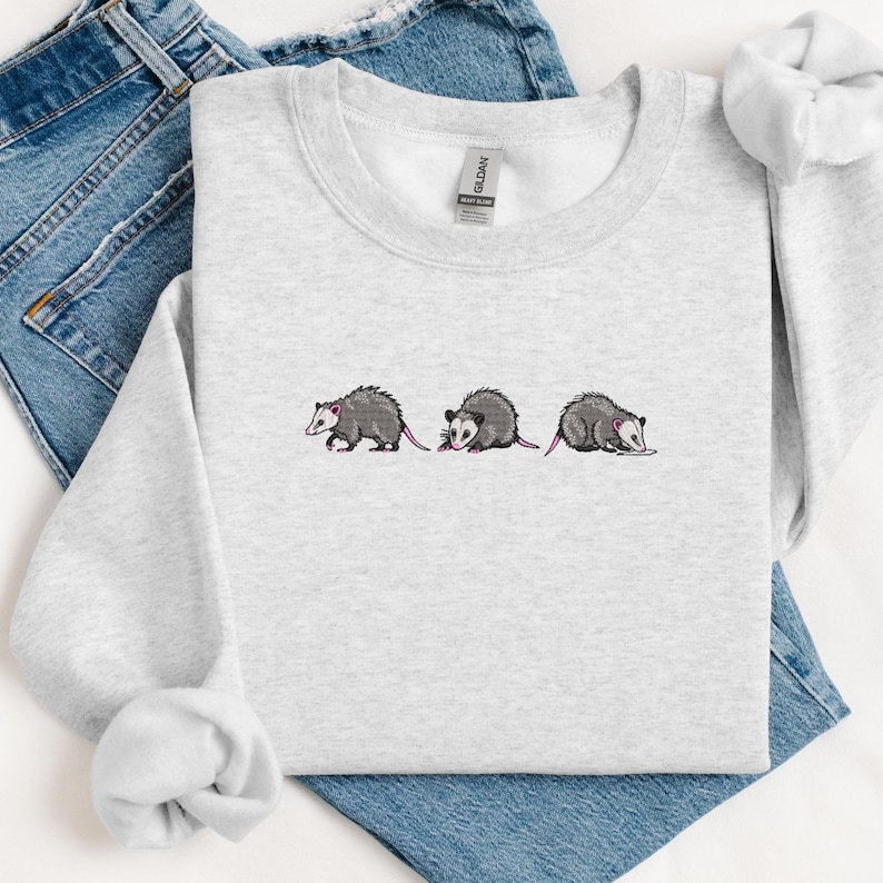May include: A gray sweatshirt with a graphic of three opossums in a line. The opossums are gray with pink ears and noses.