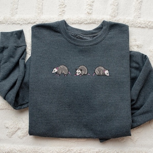 May include: A dark gray sweatshirt with three embroidered opossums in a line across the chest.