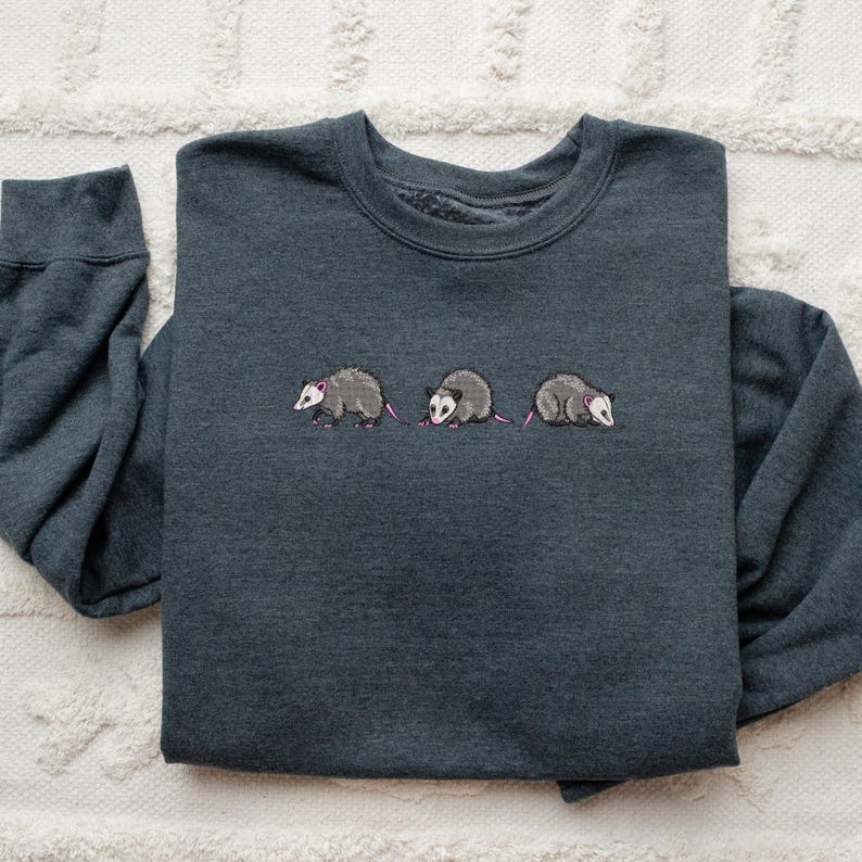 May include: A dark gray sweatshirt with three embroidered opossums in a line across the chest.