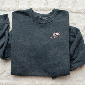 May include: A dark gray sweatshirt with a small embroidered possum on the left chest.
