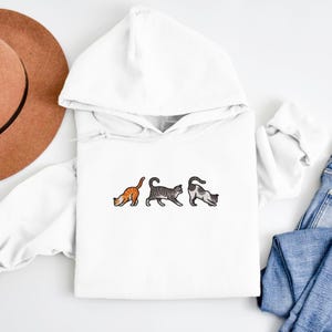 May include: White hooded sweatshirt with a graphic of three cats in a row. The cats are orange, gray, and white.