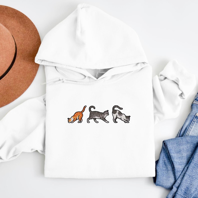 May include: White hooded sweatshirt with a graphic of three cats in a row. The cats are orange, gray, and white.