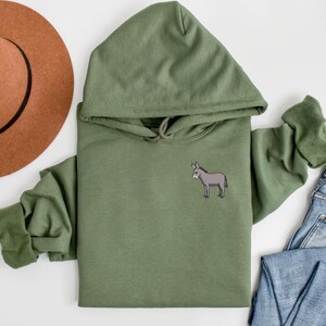 Puede incluir: Una sudadera con capucha verde con un peque&ntilde;o burro bordado en el pecho izquierdo.