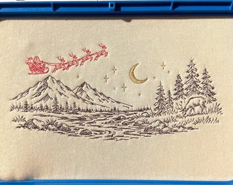 Peut inclure: Une broderie sur tissu crème dans un cadre bleu Mighty Hoop de 20,3x33 cm. Le motif montre un traîneau rouge, un croissant de lune doré, des étoiles, des montagnes, des sapins et un cerf. Le cadre porte l'inscription Keep Away From Electronic Devices.