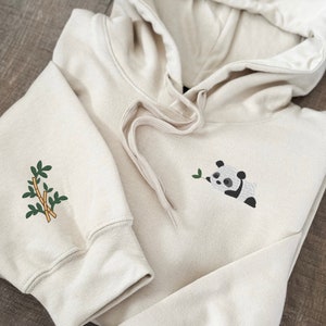 Embroidered panda bear on left chest of hoodie sweatshirt with embroidered bamboo design on the sleeve.