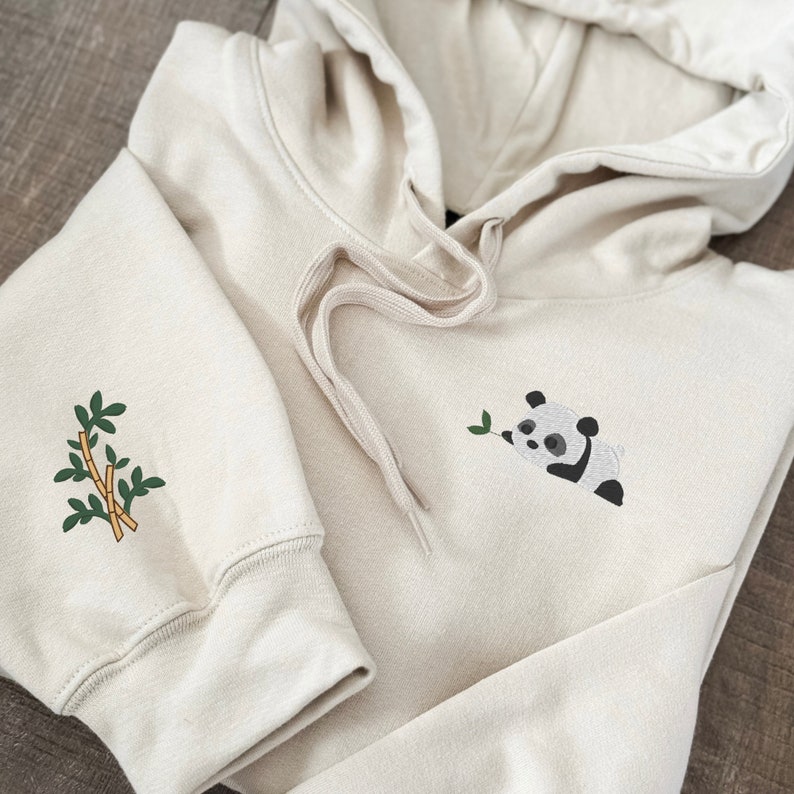 Embroidered panda bear on left chest of hoodie sweatshirt with embroidered bamboo design on the sleeve.