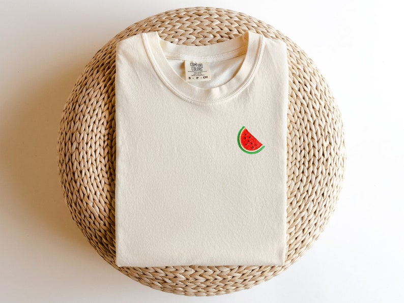 A comfort colors heavyweight garment dyed t-shirt in the color ivory with an embroidered watermelon slice on the left chest.