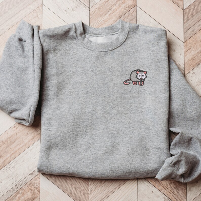 May include: A gray sweatshirt with a small embroidered opossum on the front.