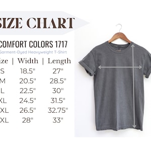 Peut inclure: Tableau des tailles pour un t-shirt lourd teint&eacute; en pi&egrave;ce Comfort Colors 1717. Le tableau indique les mesures de largeur et de longueur en pouces pour les tailles S, M, L, XL, 2XL et 3XL. Un t-shirt gris est pr&eacute;sent&eacute; suspendu &agrave; un cintre en bois.