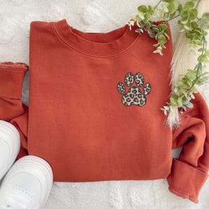 May include: A rust-colored sweatshirt with a leopard print paw print design on the front.