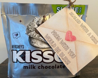 Peut inclure: Une enveloppe brune avec un cœur rose et le texte "PROM WITH YOU WOULD BE BLISS!" est attachée à un sac de chocolats au lait Hershey's Kisses. Le sac est argenté avec une étoile bleue et un cœur violet.