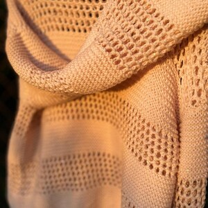 May include: A pale pink knitted sweater with a delicate openwork pattern. The sweater has a loose, relaxed fit and is made of a soft, lightweight yarn.