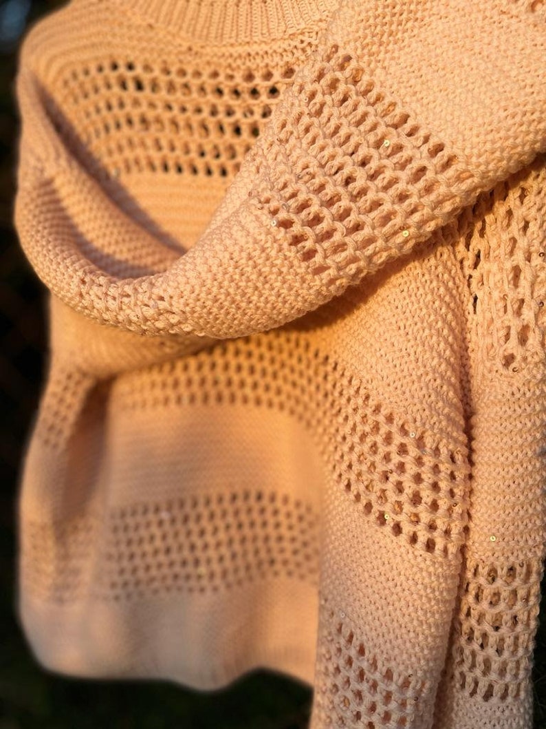 May include: A pale pink knitted sweater with a delicate openwork pattern. The sweater has a loose, relaxed fit and is made of a soft, lightweight yarn.