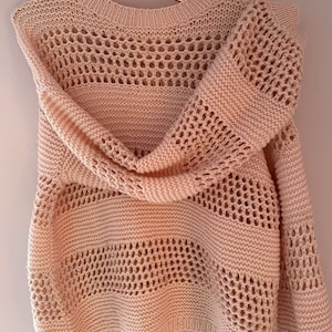 May include: A pale pink knitted sweater with a delicate openwork pattern. The sweater has a round neckline and long sleeves.