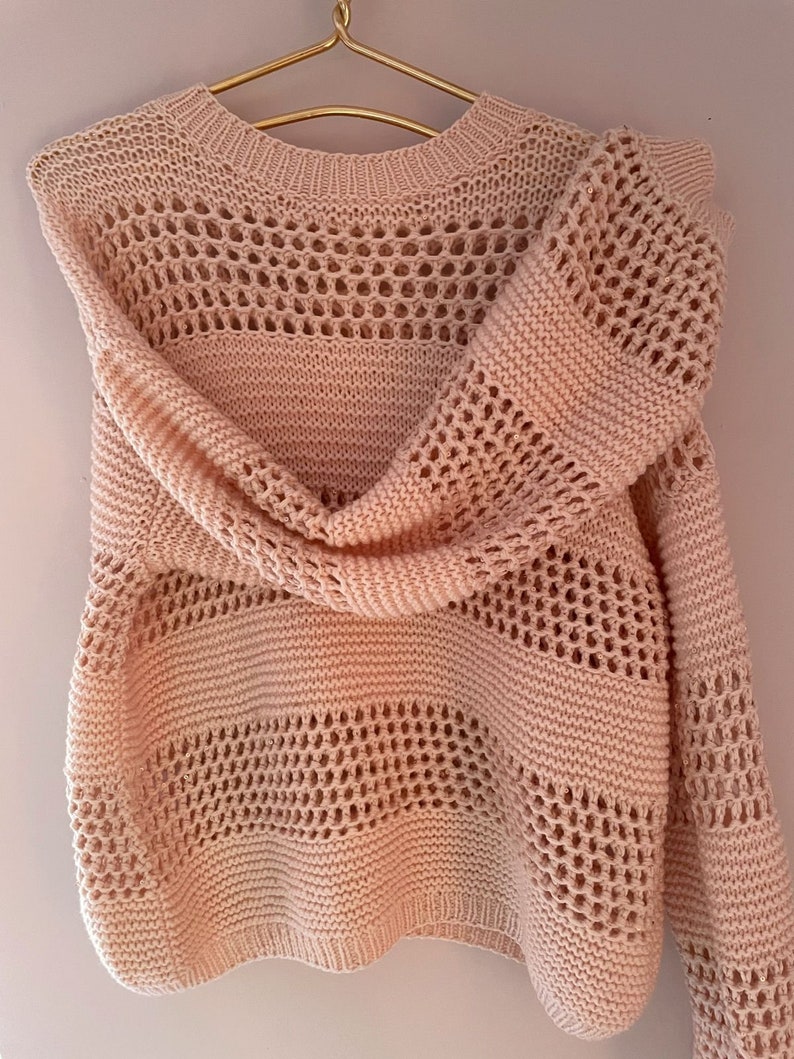 May include: A pale pink knitted sweater with a delicate openwork pattern. The sweater has a round neckline and long sleeves.