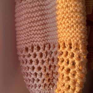 May include: A close-up of a knitted sweater with a gradient of pink and orange. The sweater has a honeycomb pattern and is decorated with small sequins.