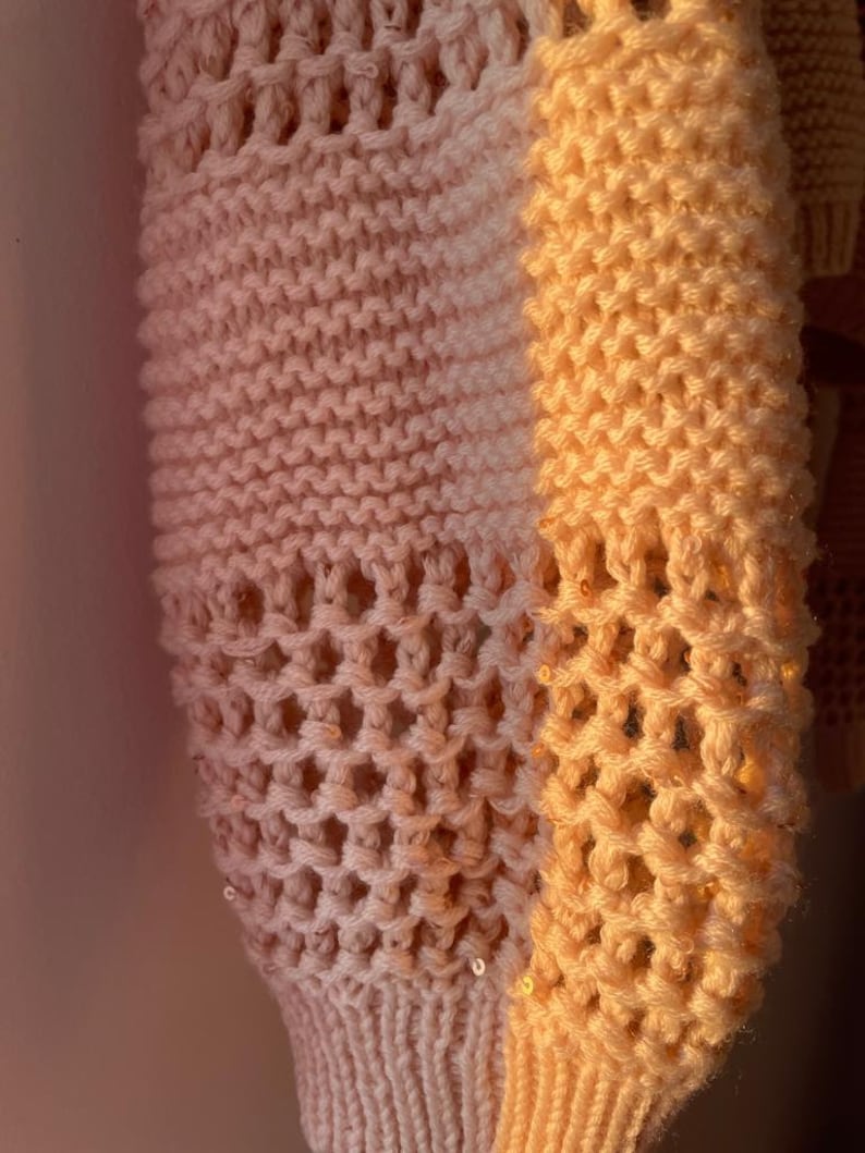May include: A close-up of a knitted sweater with a gradient of pink and orange. The sweater has a honeycomb pattern and is decorated with small sequins.
