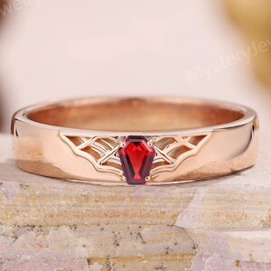 May include: Rose gold ring with a rectangular, deep red gemstone. The ring features an openwork design on the band and the text "MysteryJewelryArt". The ring is set on a textured, light brown surface.