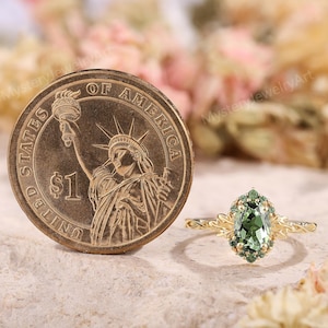 May include: A gold ring with a green gemstone and smaller green stones around it. The ring is next to a United States one-dollar coin.