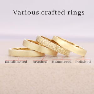 May include: Four gold rings with different textures: sandblasted, brushed, hammered, and polished. The rings are stacked at a slight angle, showcasing their varying finishes. The text "Various crafted rings" is at the top.