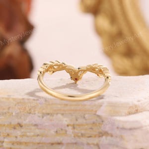 Peut inclure: Une bague dor&eacute;e avec un design incurv&eacute;. La bague pr&eacute;sente une pierre pr&eacute;cieuse rouge centrale et des d&eacute;tails complexes le long de la bande. La bague est pos&eacute;e sur un fond neutre, soulignant son design &eacute;l&eacute;gant.