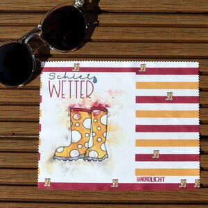 Op de afbeelding: Een witte microvezel schoonmaakdoek met rode en gele strepen. De doek heeft de tekst "Schietf Wetter" en een cartoon afbeelding van gele regenlaarzen met witte stippen. De rechter benedenhoek van de doek heeft de tekst "nordlicht".