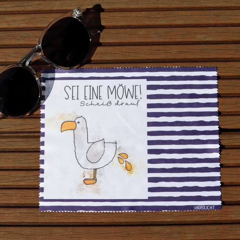 Op de afbeelding: Een witte microvezel schoonmaakdoek met blauwe en witte strepen. De doek heeft een cartoon zeemeeuw met de tekst "Sei eine M&ouml;we! Schei&szlig; drauf" en het woord "NORDLICHT" in de rechterbenedenhoek.