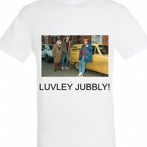 May include: A white t-shirt with a photo of three men standing in front of a yellow van. The van has the words "Trigger's Broomstick" written on the side. The text "LUVLEY JUBBLY!" is printed below the photo.