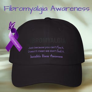 Puede incluir: Gorra de béisbol negra con el texto "Fibromialgia" y "Solo porque no puedes verlo, no significa que no lo sintamos". Una cinta y una mariposa moradas están unidas a la gorra. Para la concienciación sobre la fibromialgia.