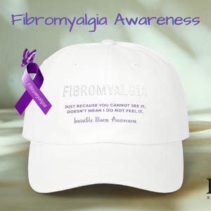 Puede incluir: Una gorra de béisbol blanca con la palabra "Fibromialgia" bordada en la parte delantera. Una cinta morada con una mariposa y las palabras "Concienciación sobre la fibromialgia" están adjuntas al costado. La gorra también tiene el texto "SÓLO PORQUE NO PUEDES VERLO, NO SIGNIFICA QUE NO LO SIENTA, Concienciación sobre enfermedades invisibles."