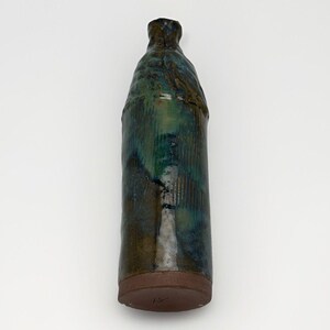 May include: A handcrafted ceramic bottle with a textured, glazed surface. The bottle features a gradient of green and blue hues, with a dark brown base and neck. The design includes vertical lines and a unique, organic shape.