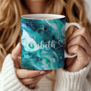 May include: White ceramic mug with a teal and gold abstract marble design. The mug has the name "elizabeth" written in white cursive with a small heart symbol.