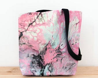 May include: A pink, black, and white tote bag with a marbled design. The bag has black canvas straps.