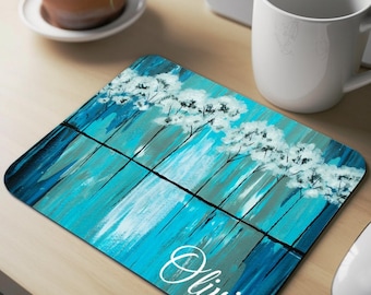 Pode incluir: Um tapete de rato personalizado com uma pintura abstrata azul e branca de árvores refletidas na água. O nome "Olivia" está escrito em itálico branco na parte inferior do tapete.