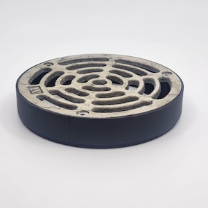 May include: A round, black drain grate with a silver, circular, patterned top. The grate is made of metal and has a raised edge.
