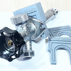 May include: A gray plastic adapter with the text "Wilder Designs" printed on it. The adapter is designed to fit over a standard outdoor water faucet. The adapter is shown with a black handle and a silver faucet.
