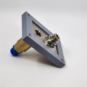 K&ouml;nnte beinhalten: Eine graue, quadratische Metallkomponente mit einem Messinganschluss und einer blauen Kappe. Die Komponente hat ein silberfarbenes Mittelteil mit einem Gewindeende. Der Messinganschluss erstreckt sich von dem grauen Quadrat.