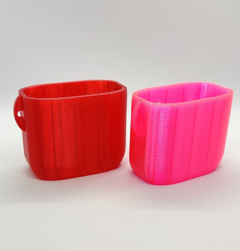 May include: Two small, rectangular containers, one red and one pink. Both containers have a ribbed texture and a rounded edge.