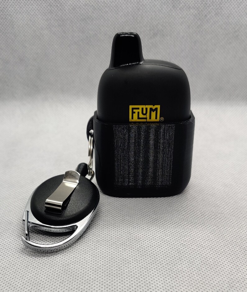 May include: Black FLUM vape pod case with a black retractable keychain. The case has a textured surface and the FLUM logo is printed in yellow.