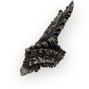 May include: A silver-toned metal sculpture with intricate details. The sculpture features a series of overlapping, leaf-like shapes that create a sense of movement and depth. The sculpture is abstract and non-representational, with a focus on form and texture.