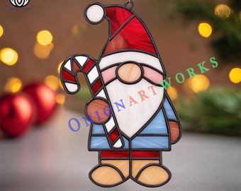May include: Stained glass Christmas gnome ornament with a red hat, blue coat, and a candy cane. The gnome has a white beard and a pink nose. The ornament is outlined in black and has the text "Onion Art Works".