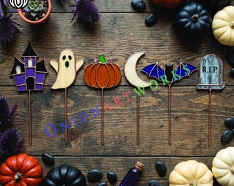 May include: A set of six stained glass Halloween plant stakes featuring a purple haunted house, a cream ghost, an orange pumpkin, a crescent moon, a blue bat, and a gray tombstone with the text R.I.P. each on a thin metal rod.