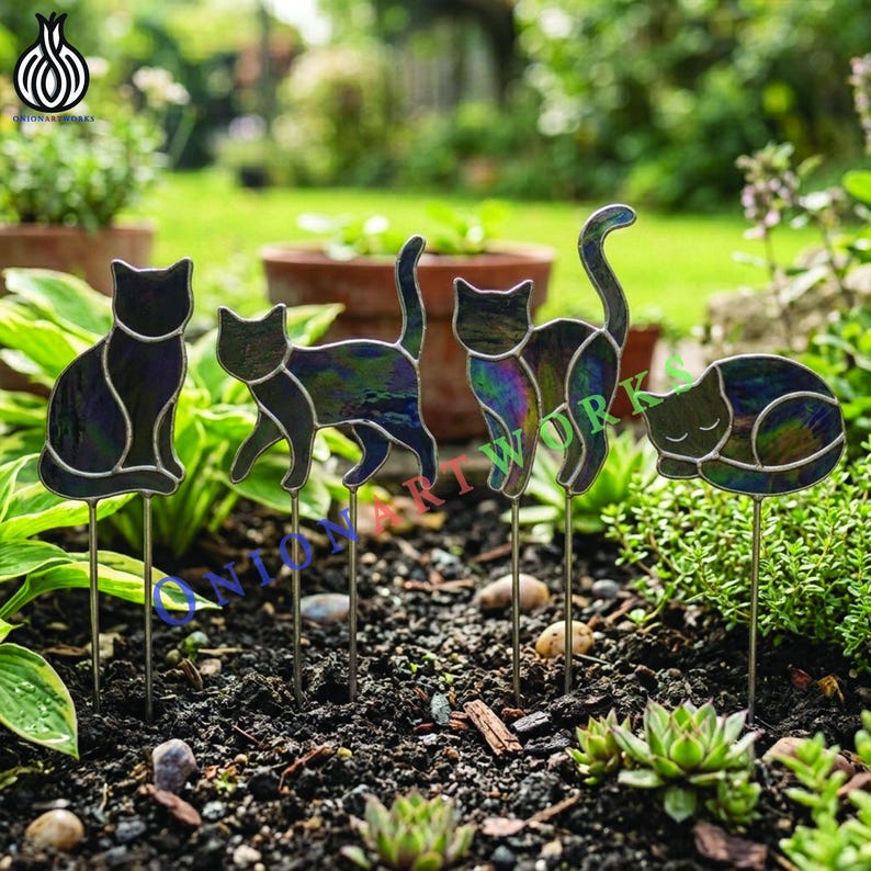 May include: Four iridescent stained glass cat garden stakes in various poses, including sitting, walking, standing, and sleeping. Each cat figure is crafted with dark, shimmering glass panels outlined in metal, mounted on thin metal rods for display.