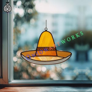 May include: Stained glass sombrero in shades of yellow, orange, and white, hanging by a chain. The hat features a decorative band and is set against a blurred window background. The text "ONION ART WORKS" is visible.