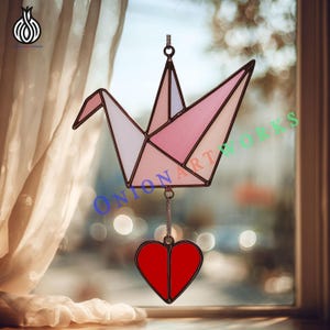 May include: A stained glass origami crane suncatcher with a red heart pendant. The crane features shades of pink and white, with a black outline. The heart is a solid red color, and the piece hangs from a chain.