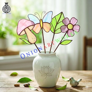Puede incluir: Un jarrón de cerámica blanca con un diseño de flor de loto contiene flores de vidrieras de colores, una mariposa y una seta. La imagen incluye el texto "ONIONARTWORKS". Un pequeño pájaro de cerámica está sobre una mesa de madera.