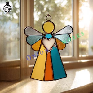 May include: A colourful stained glass angel decoration with a heart-shaped centre and wings. The angel features yellow, orange, blue, and silver glass panels, framed with a dark metal. It has a hanging loop and the text "ONIONARTWORKS".