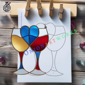 May include: A stained glass wine glass design with a heart-shaped centre in blue, red, and yellow. The design is displayed on white paper with a line drawing of a wine glass. The paper is held by wooden clips.