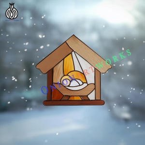 May include: A stained glass nativity scene in a wooden stable. The artwork features a baby in a manger, with warm yellow and orange hues. The roof and base are brown, and the background is a snowy scene.